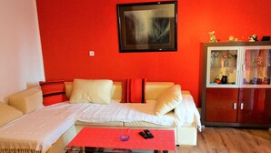 A living room with a red wall, a beige sofa, a glass coffee table, and a cabinet with glass doors. - Bright and Stylish Apartment With Balcony and Sea View (Crikvenica)