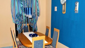 A dining area with a wooden table and chairs, a blue wall, a clock, and a decorative item on the wall. - Bright and Stylish Apartment With Balcony and Sea View (Crikvenica)