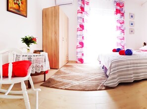 A bedroom with a bed, a chair, a small table with books, a wardrobe, and a window with curtains. - Seafront Chic Crikvenica Apartments (Crikvenica)