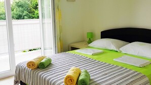 A hotel room with a bed, a nightstand, a green lamp, and a view of greenery outside. - Seafront Chic Crikvenica Apartments (Crikvenica)