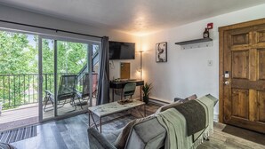 A living room with a sofa, a table, a TV, and a wooden door. - The Copper Bungalow (#110) | Walk to Purgatory Ski Lift - Deck, Fireplace (Durango)
