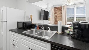 Una cocina moderna con encimera negra, pileta de acero inoxidable, microondas, cafetera Keurig y televisor de pantalla plana montado en la pared.