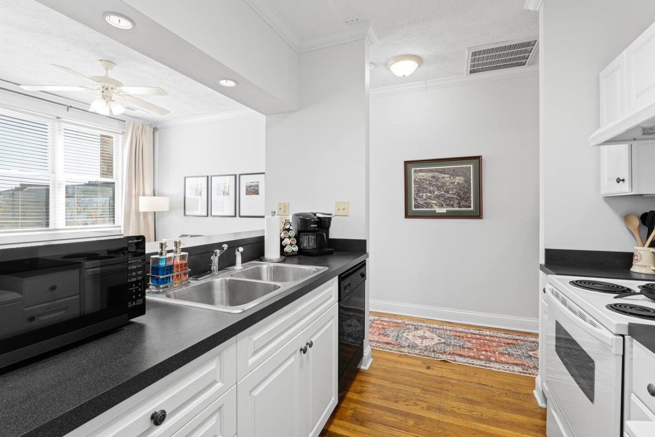 A modern kitchen with a black countertop, stainless steel sink, and white cabinetry.