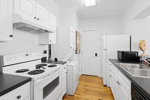 Una cocina con armarios blancos, estufa, microondas y pileta.