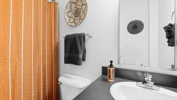 With stylish décor and modern touches, this bathroom features a shower/tub combo with a warm, inviting curtain. Thoughtful accents like the woven wall art add a touch of character, making this space both functional and visually appealing.