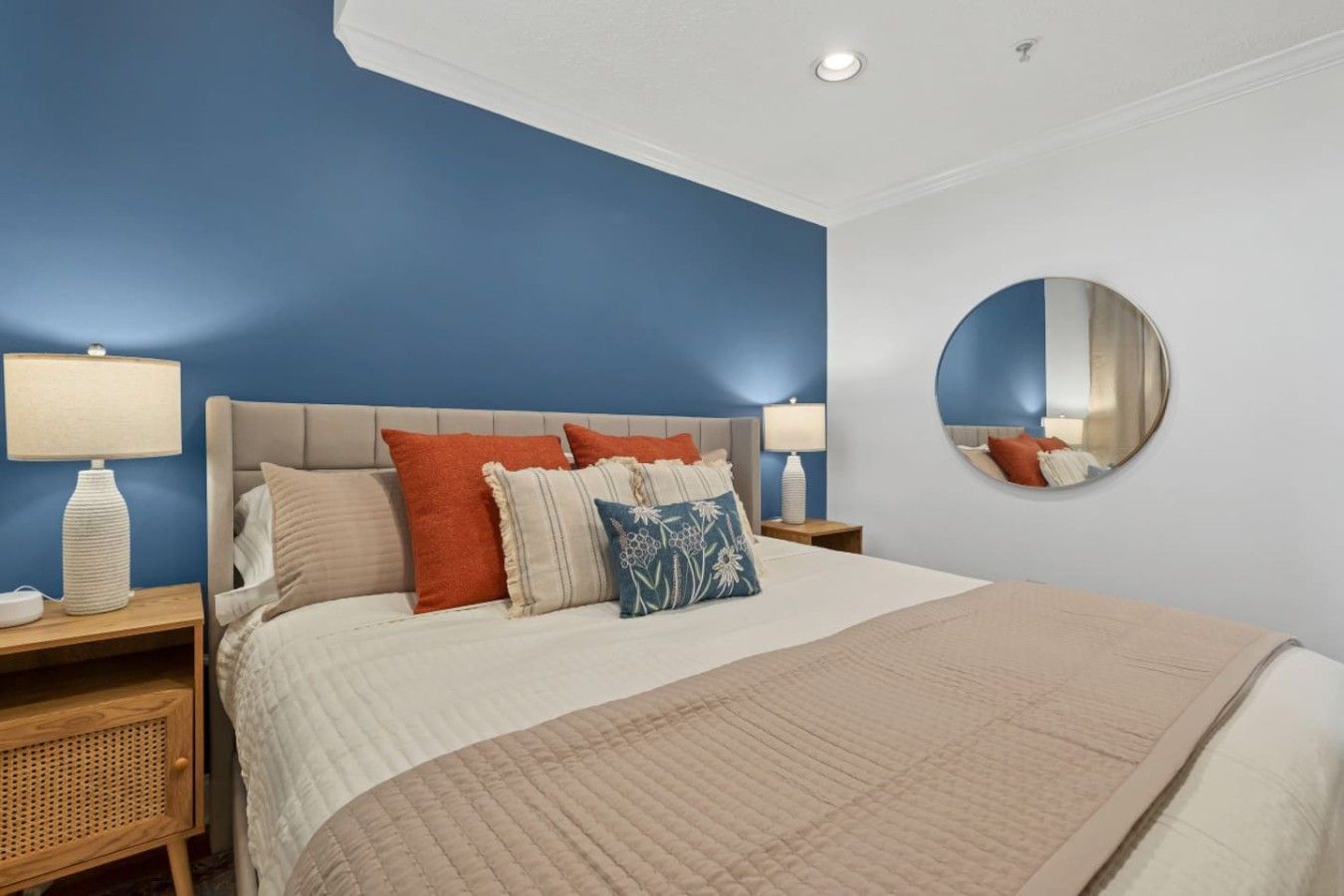 A bedroom with a bed, two bedside tables, a round mirror, and a blue accent wall.