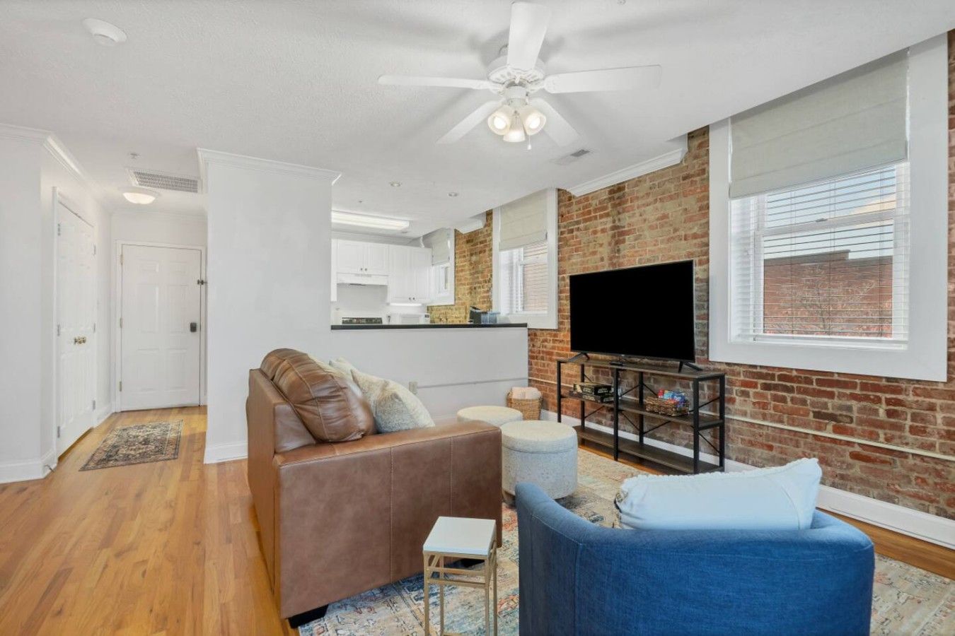 A modern living room with a brown leather sofa, a blue armchair, a small table, and a flat-screen TV mounted on a brick wall.