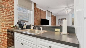 Eine Küche mit Backsteinwand, einer Kaffeemaschine, einem Spülbecken und einem Deckenventilator.