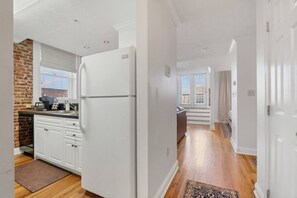 Una cocina con refrigerador, gabinetes blancos y pared de ladrillo.