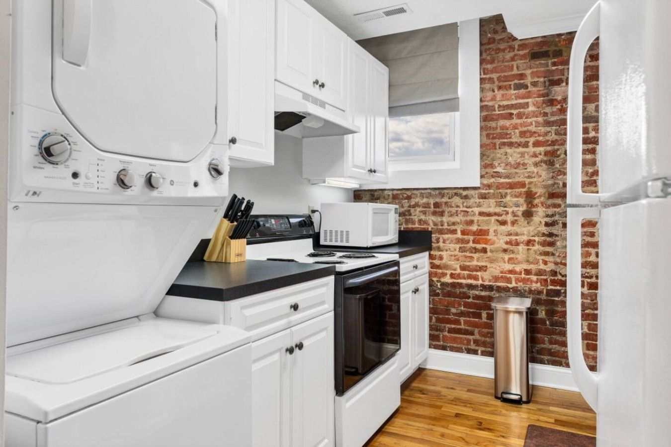 Una cucina compatta con mobili bianchi, un forno a microonde, un forno e un muro in mattoni.