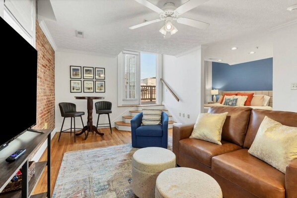 A modern living room with a television, seating area, and a staircase leading to an upper floor.