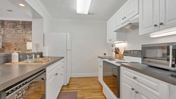 A modern kitchen with white cabinetry, a built-in oven, a microwave, and a brick accent wall.