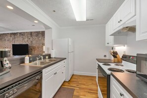 Une cuisine moderne avec des meubles blancs, un évier en acier inoxydable, un four encastré et un mur décoratif en briques.