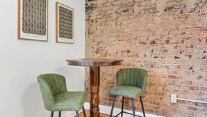 Ein Zimmer mit Backsteinwand, zwei gepolsterten grünen Sesseln und einem runden Holztisch.