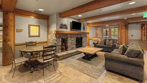 A spacious living area with a stone fireplace, wooden beams, a dining table with chairs, and a sofa.