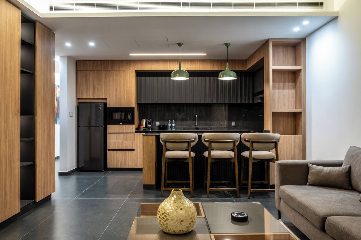 A modern kitchen with wooden cabinets, a black refrigerator, and two bar stools.