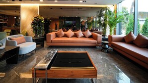 Een moderne woonkamer met een bank, fauteuils en een salontafel. Achterin staat een televisie, en grote ramen zorgen voor natuurlijk licht.