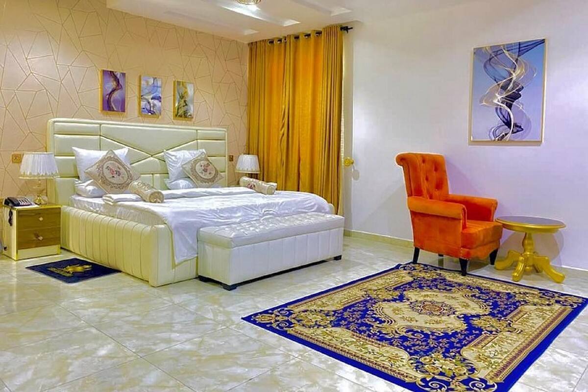 A hotel room with a large bed, a chair, a small table, and artwork on the walls.
