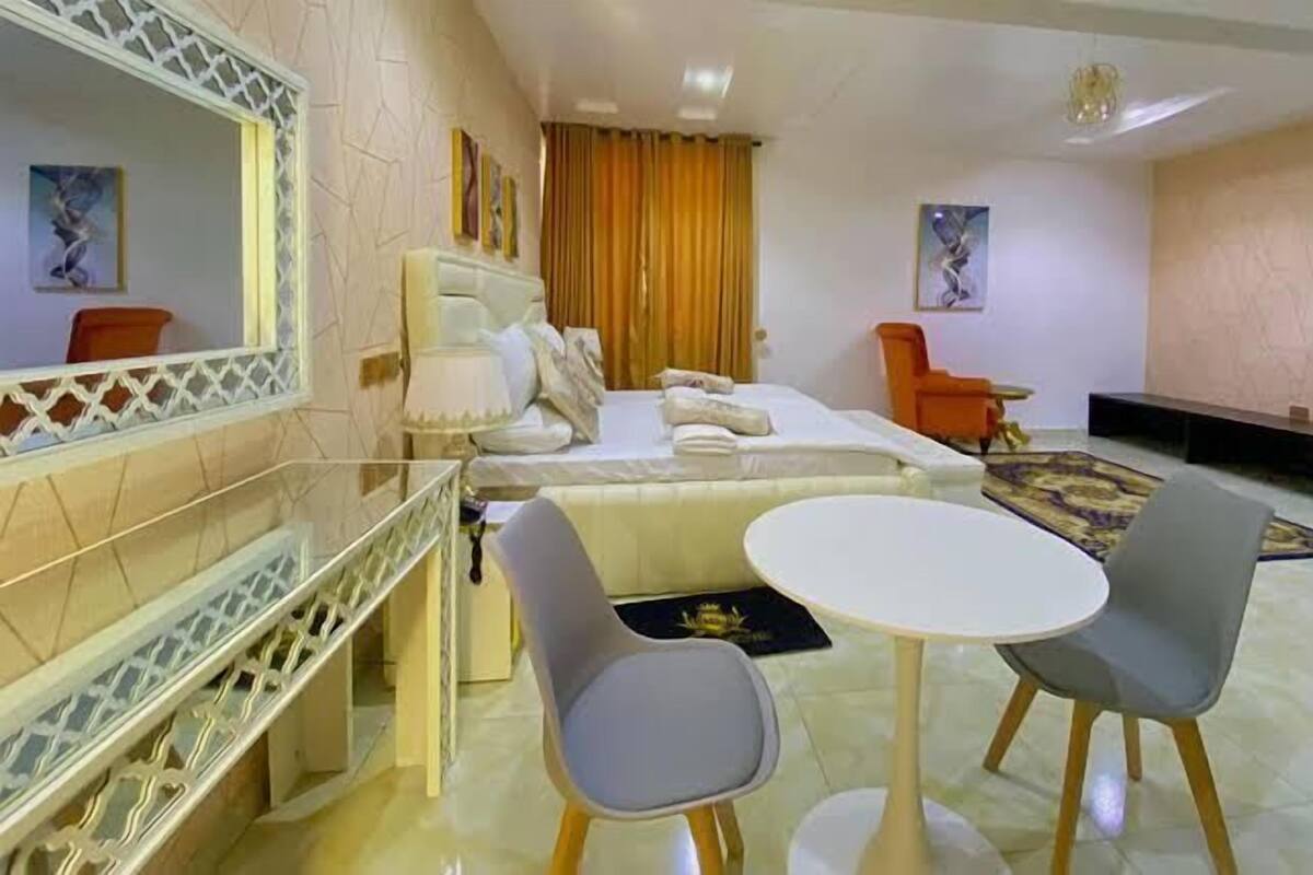 A hotel room with a bed, a desk, two chairs, a small table, and a TV.