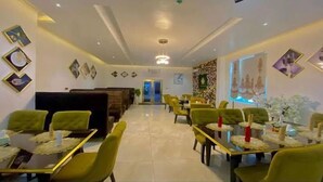 A restaurant with green upholstered seating, a reception area, and decorative wall art. - Hogis Luxury Suites and Hotel (Calabar)