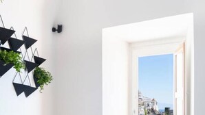 Habitación minimalista con una mesa redonda, dos sillas, un taburete azul, un adorno geométrico en la pared y una ventana con vista al mar.