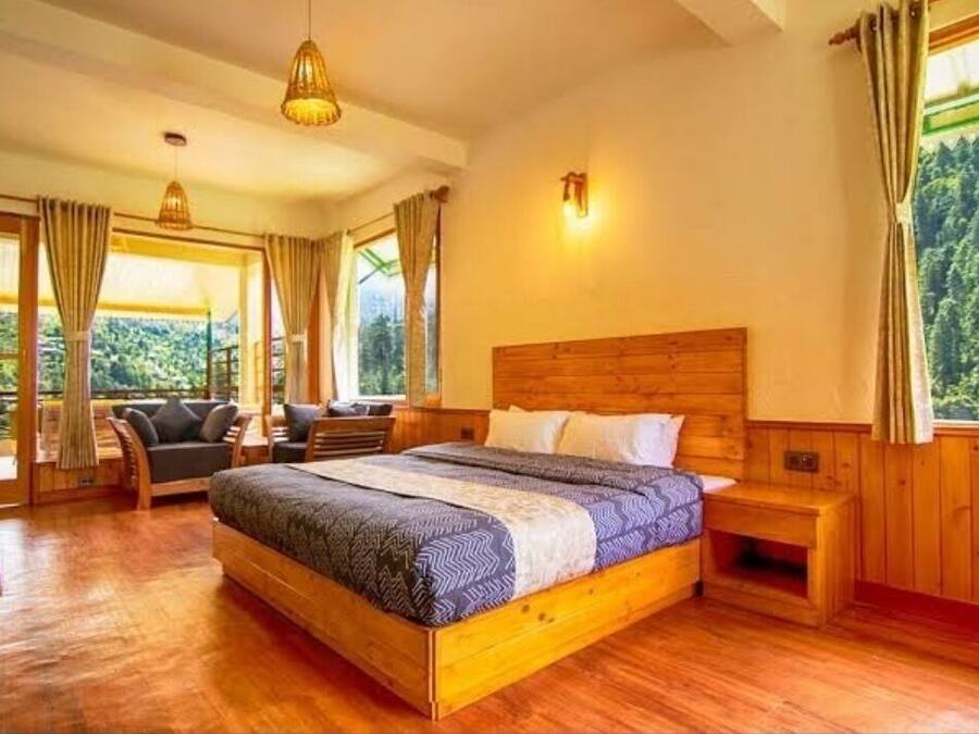 Un dormitorio con estructura de madera, con una cama grande, un sofá y vistas a un bosque por la ventana.