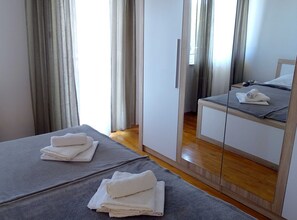 Een hotelkamer met twee bedden, elk voorzien van een grijze deken en witte handdoeken. Er hangt een spiegel aan de muur, en de vloer is van hout.