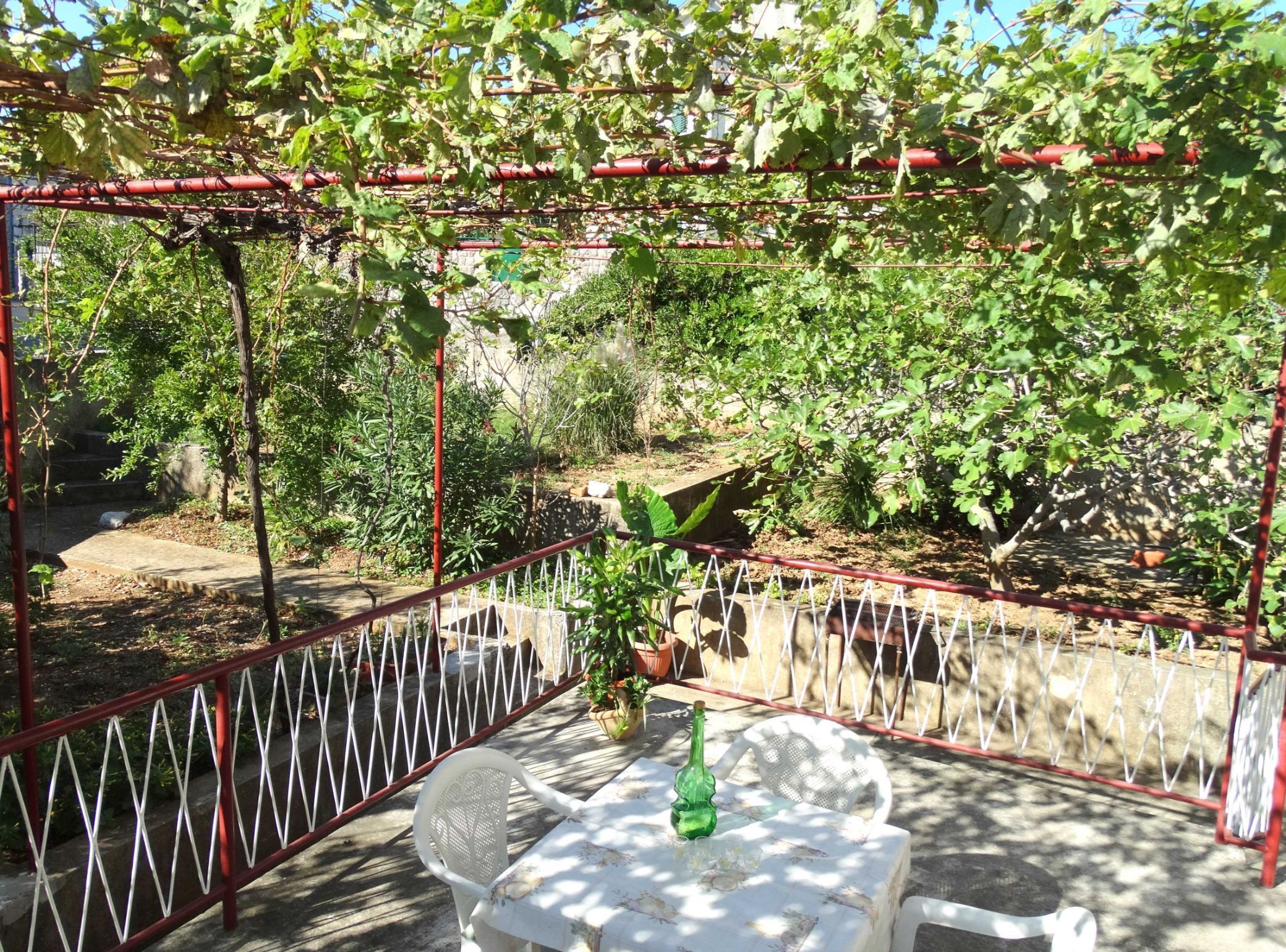 An outdoor seating area with a table and chairs, surrounded by a metal fence and greenery.