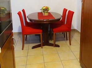 Un comedor con una mesa redonda, cuatro sillas rojas y un jarrón de flores.