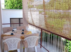Un balcón con una mesa lista para dos, sillas blancas y un mosquitero.