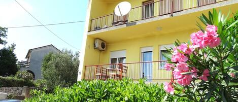A yellow building with a balcony, air conditioning unit, and a satellite dish.