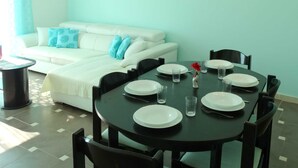 Un coin repas avec une table ronde dressée pour quatre personnes, entourée de chaises noires. Un canapé blanc avec des coussins bleus est placé contre le mur turquoise.