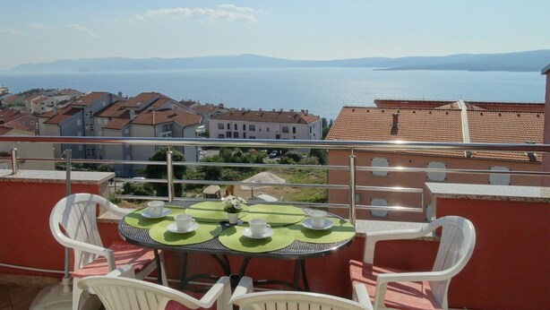 Un balcon avec une table dressée pour deux personnes, offrant une vue sur une ville côtière et la mer.