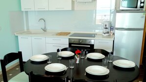 Une cuisine moderne avec des meubles blancs, une table à manger noire pour six personnes et un four à micro-ondes placé au-dessus de la cuisinière.