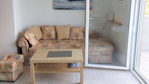 Ett vardagsrum med en soffa, ett soffbord och en glasdörr som leder ut till ett utomhusområde.