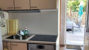 Ett kompakt kök med diskmaskin, diskho och ett fönster med utsikt över en uteplats med utomhusmöbler.