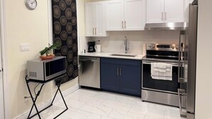 Una cucina moderna con mobili bianchi, elettrodomestici in acciaio inossidabile e un forno a microonde su un mobiletto.
