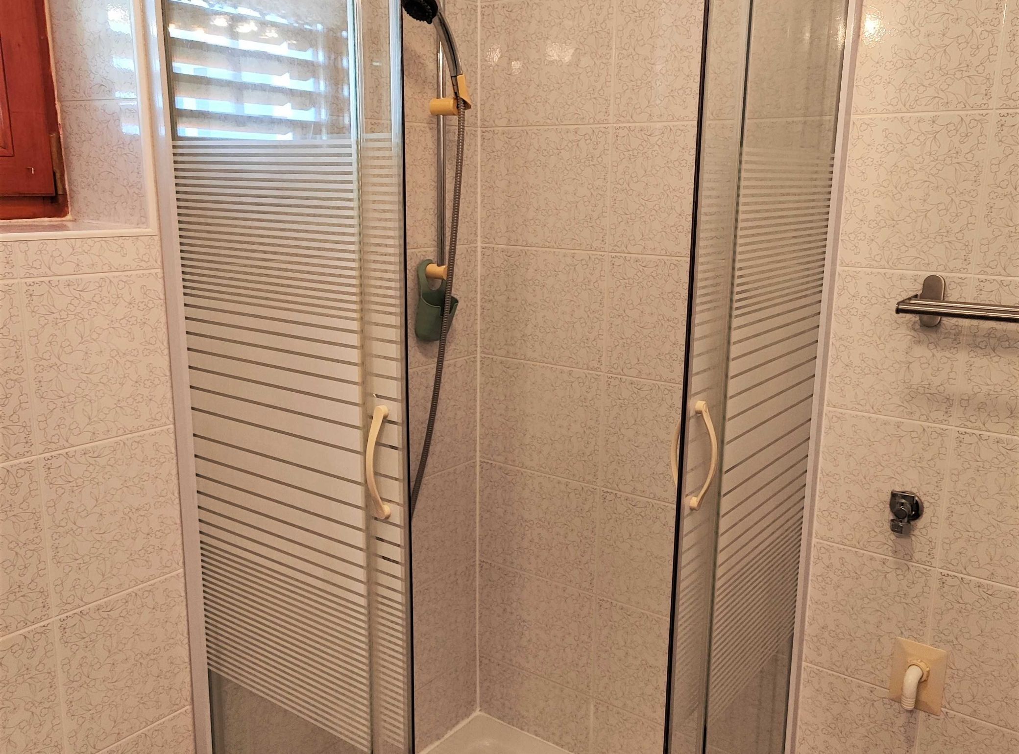A shower with a glass door, a towel rack, and a toilet paper holder.