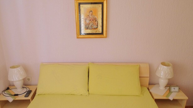 Een slaapkamer met een bed, twee nachtkastjes, twee lampen, een klok en een ingelijst beeld aan de muur.