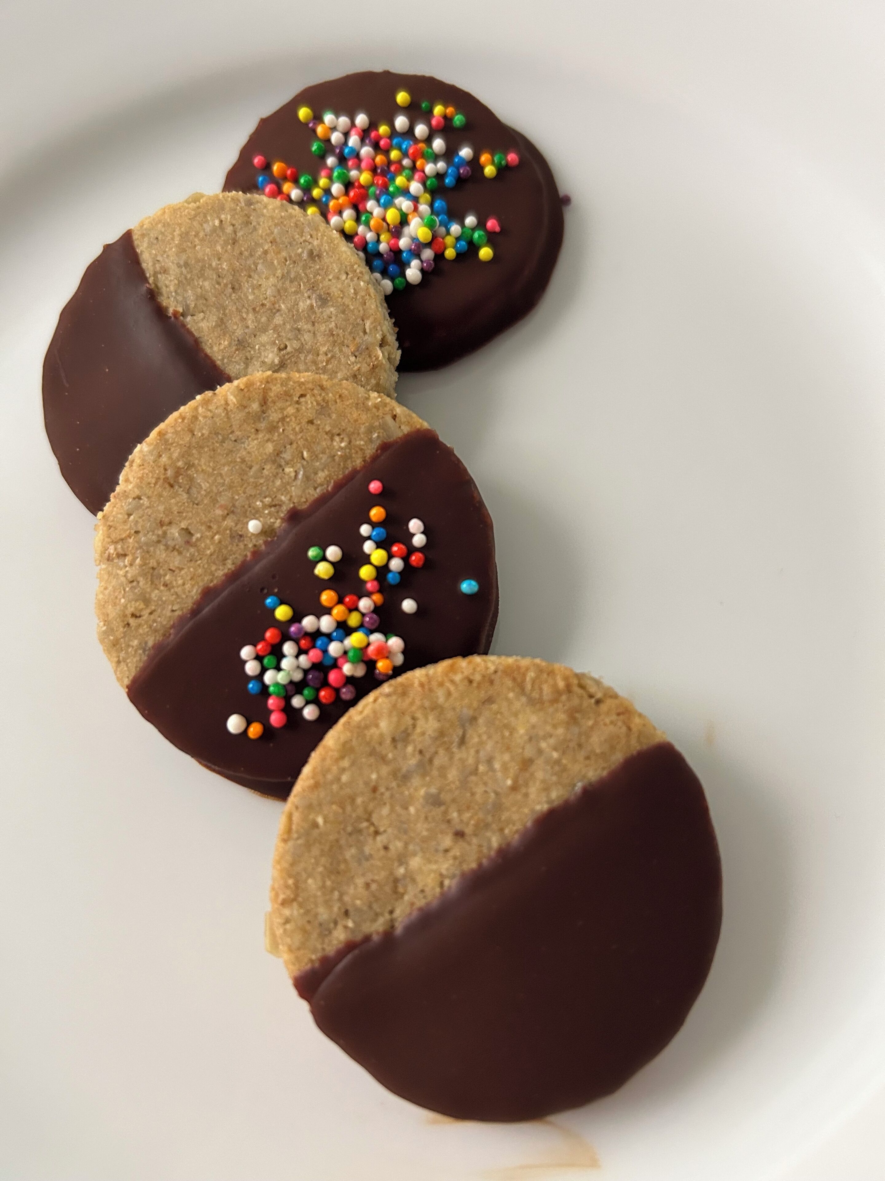 Four chocolate-covered cookies with colorful sprinkles on a white plate.