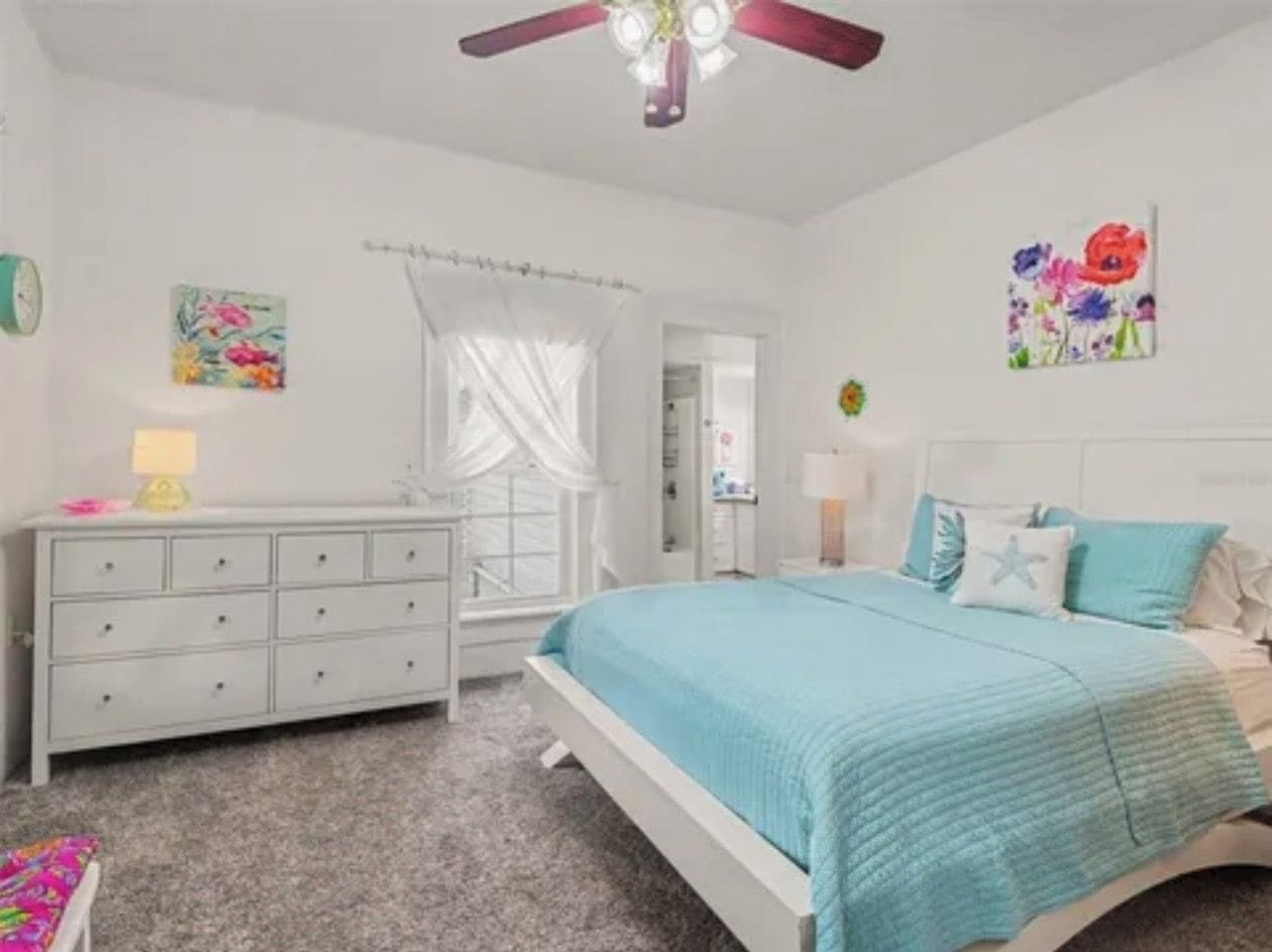 Un dormitorio con cama, cómoda, ventilador de techo y obras de arte en las paredes.