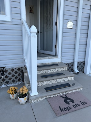 Guests enter through a charming entrance with a welcoming sign and potted plants.