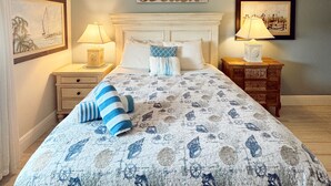 A bedroom with a bed, a ceiling fan, a nightstand, a lamp, a framed picture, and a wall sign.