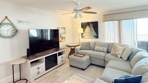 A modern living room with a sectional sofa, a flat-screen TV, a ceiling fan, and a small side table.