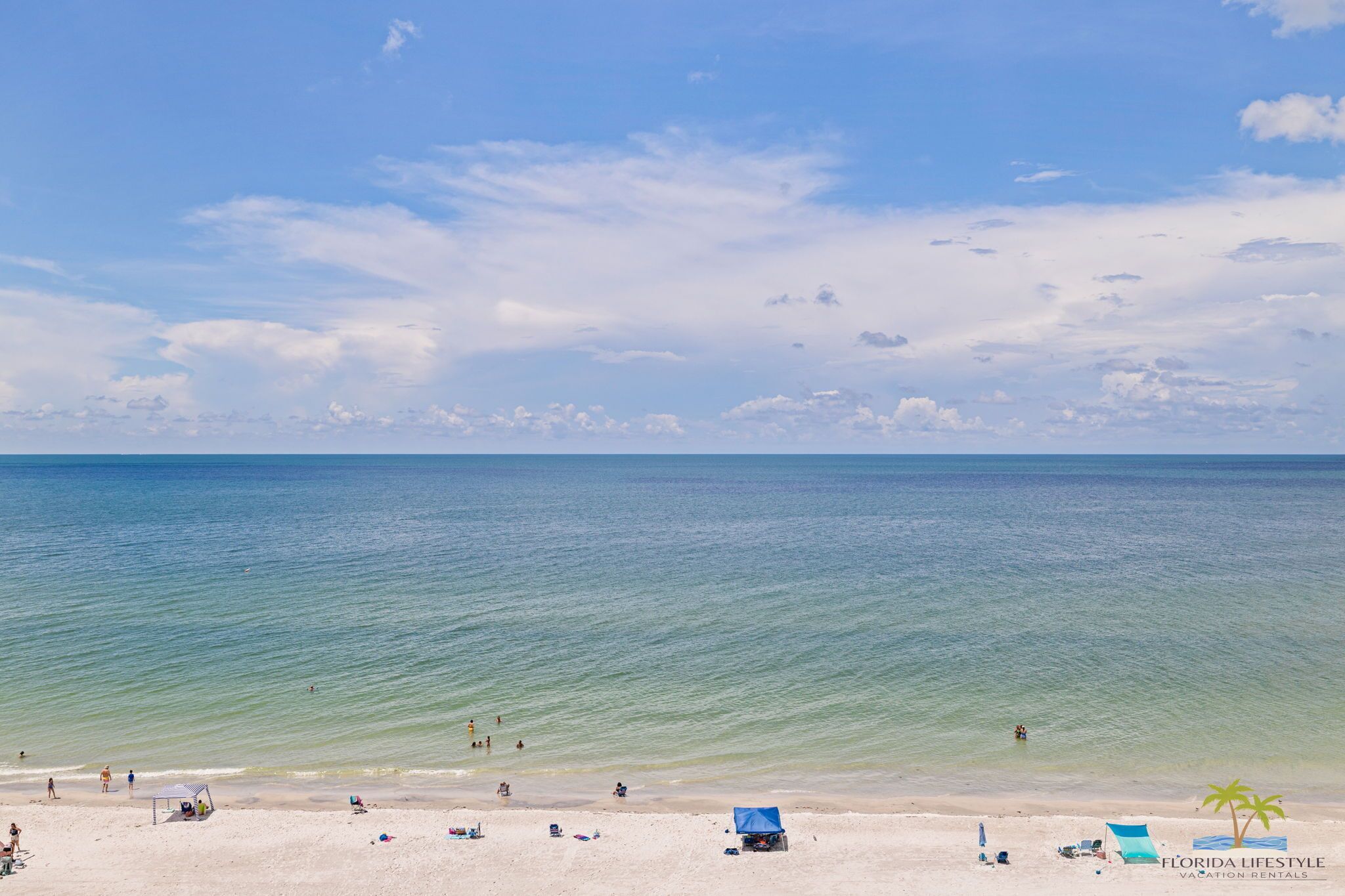 Une plage avec un ciel dégagé, une eau calme et quelques personnes qui profitent du soleil. Des chaises de plage et des parasols sont installés pour permettre aux gens de se prélasser au soleil.