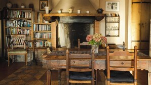 A cozy dining room with a wooden table, chairs, a fireplace, and a bookshelf filled with books.