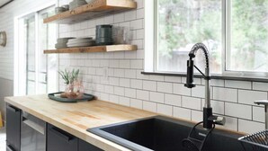A kitchen with a wooden countertop, a black sink, and a window with a view of greenery. - Bluebird Day - Lodgepole House: Spacious 3BR retreat in scenic Bend, OR, perfect for families. (Bend)