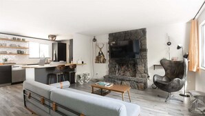 A modern living room with a stone fireplace, a grey sofa, and a black chair. - Bluebird Day - Lodgepole House: Spacious 3BR retreat in scenic Bend, OR, perfect for families. (Bend)