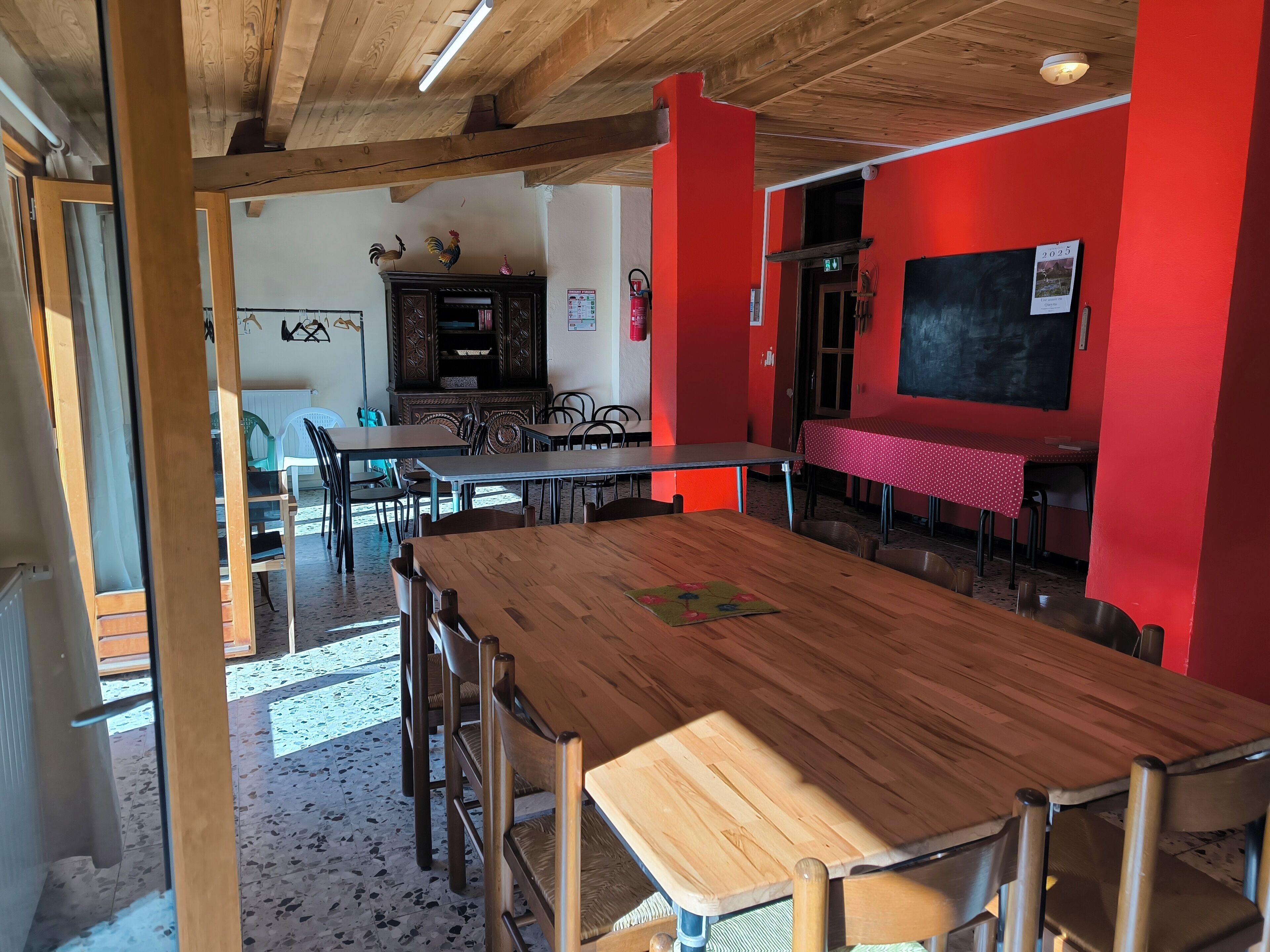A dining area with wooden tables and chairs, a red wall, and a blackboard.