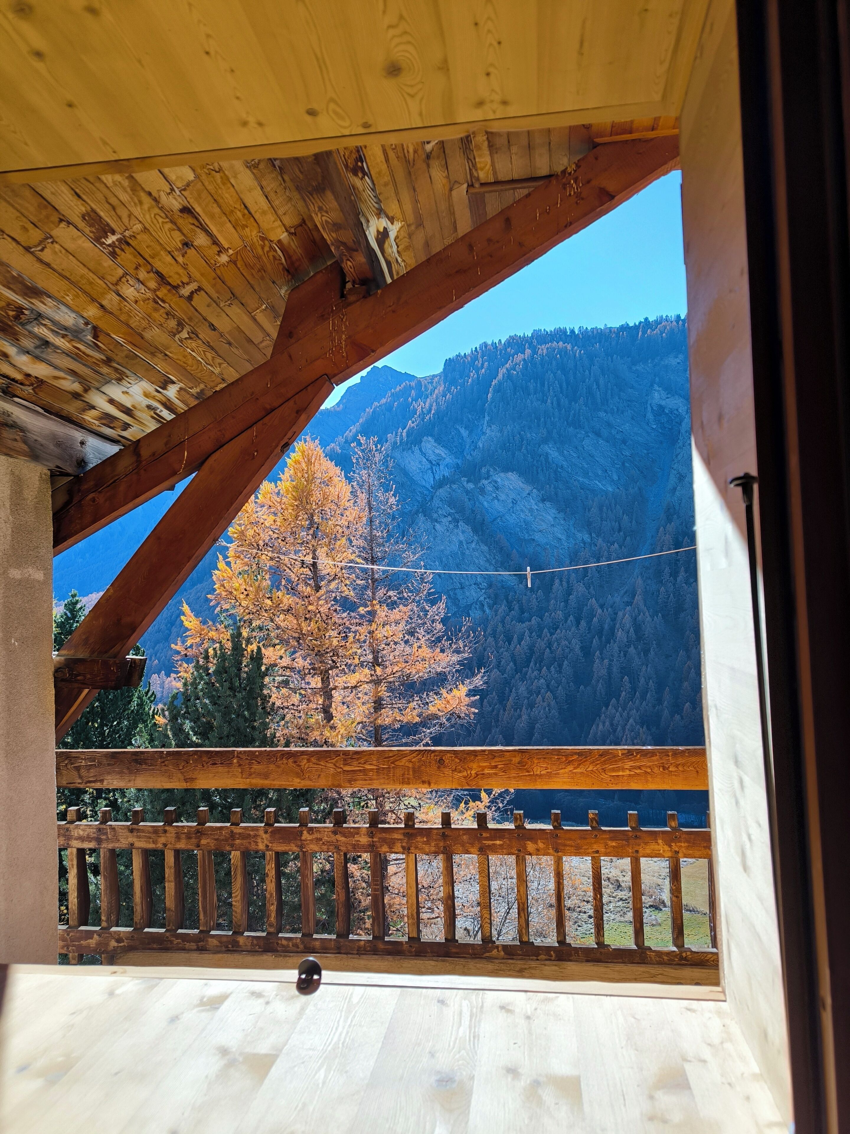 Un balcon en bois offrant une vue sur les arbres aux couleurs automnales et une chaîne de montagnes.